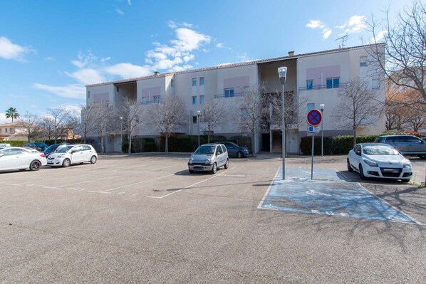 A parking lot with several cars, a no parking sign, and a building with multiple floors and balconies.