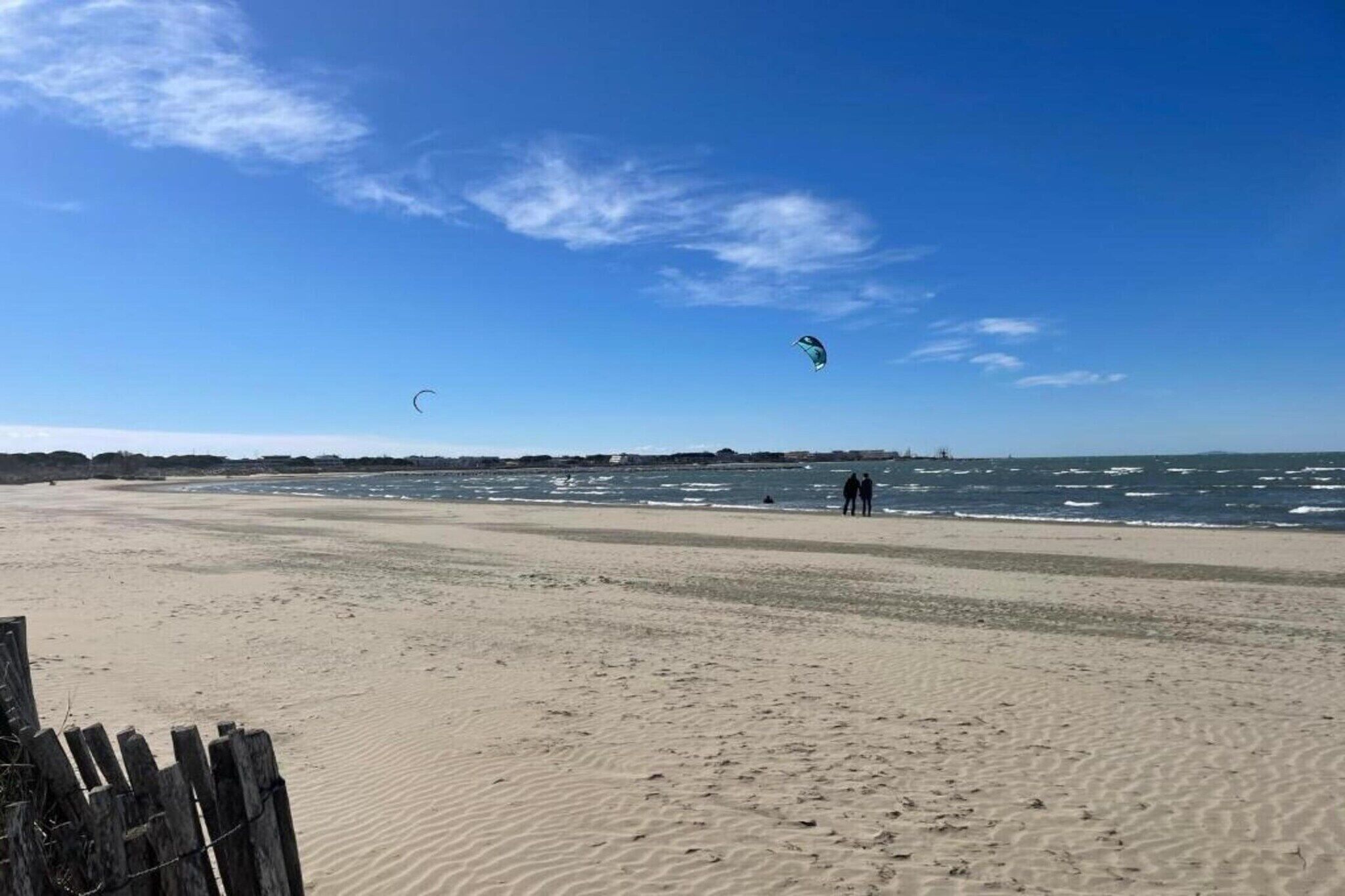 Une plage avec une clôture en bois, un rivage sablonneux et un ciel bleu dégagé.