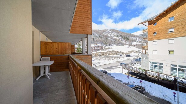 A balcony with a wooden railing overlooking a snowy landscape and a building with multiple windows.