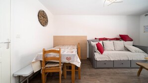 A compact bedroom with a wooden bed, a small table with a heart-patterned tablecloth, and a wall clock.