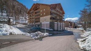 A multi-story building with balconies, a parking area, and a snow-covered landscape.