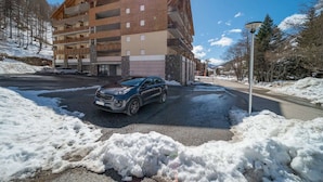 A multi-story building with balconies, a car parked in front, and snow on the ground.