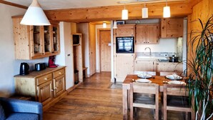 A compact kitchen with wooden cabinets, a dining table set for two, and a hanging light fixture.