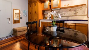 Une cuisine compacte avec des meubles en bois, une table à manger en verre et une orchidée en pot.