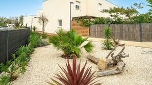 Un bâtiment moderne doté d’un toit plat, d’une clôture en bois et d’un jardin de gravier agrémenté de différentes plantes.