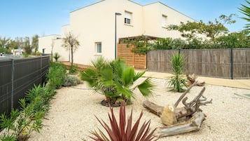 A modern building with a flat roof, a wooden fence, and a gravel garden with various plants.