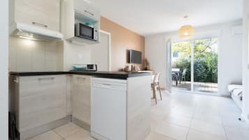 A modern kitchen with a dishwasher, microwave, and a TV above the counter. There is a dining area with a table and chairs, and a sliding glass door leading to a balcony.
