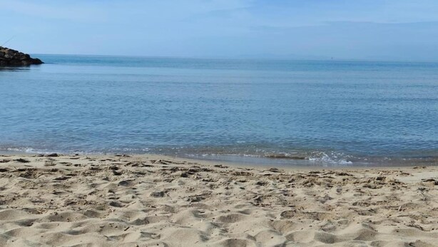 Une plage de sable fin, avec une eau d’un bleu limpide et un promontoire rocheux sur la gauche.