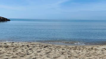 A sandy beach with clear blue water and a rocky outcrop on the left.