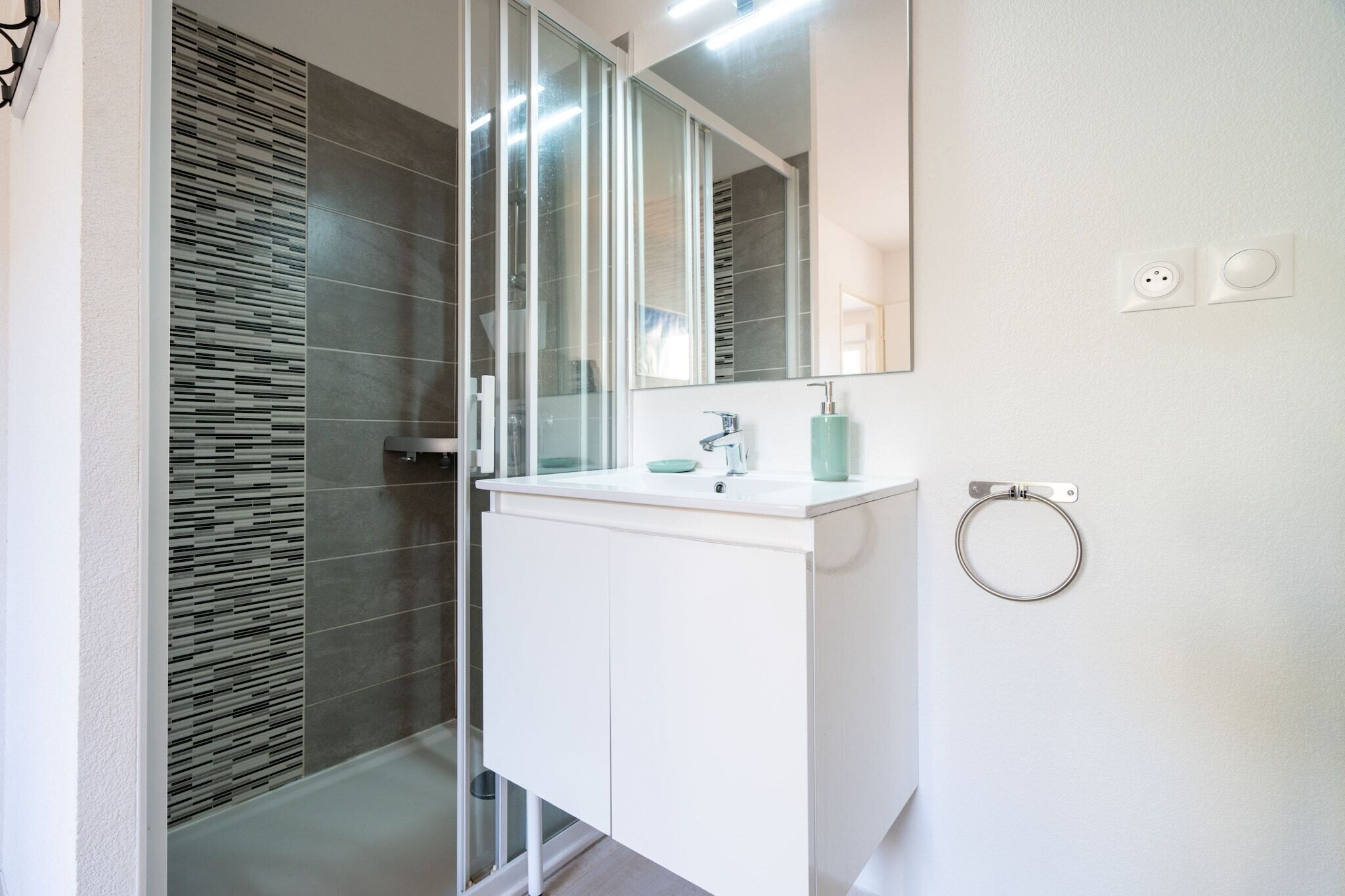 A modern bathroom with a glass shower enclosure, a white vanity, and a large mirror.