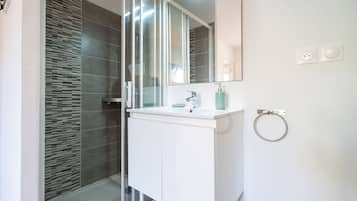 A modern bathroom with a glass shower enclosure, a white vanity, and a large mirror.