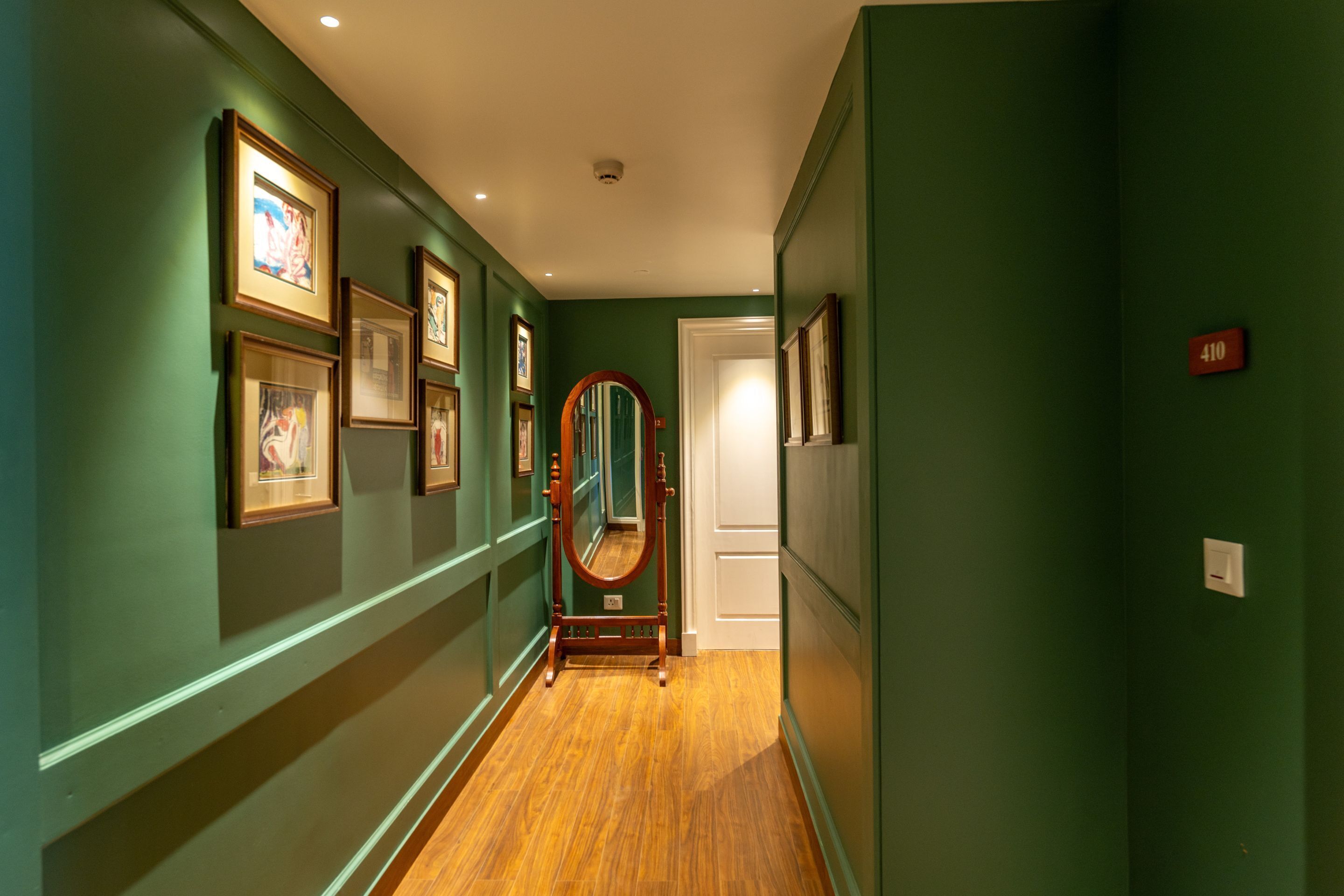 A hallway with green walls, wooden flooring, and framed pictures on the walls.