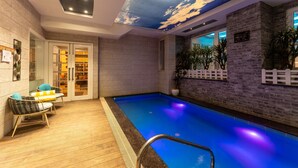 An indoor swimming pool with a wooden deck, wicker chairs, and a ceiling mural. - Moustache Mussoorie (Uttarakhand)
