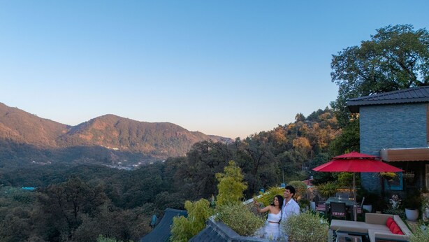 A couple on a rooftop terrace with a view of mountains and a dining area with outdoor furniture. - Moustache Mussoorie (Uttarakhand)