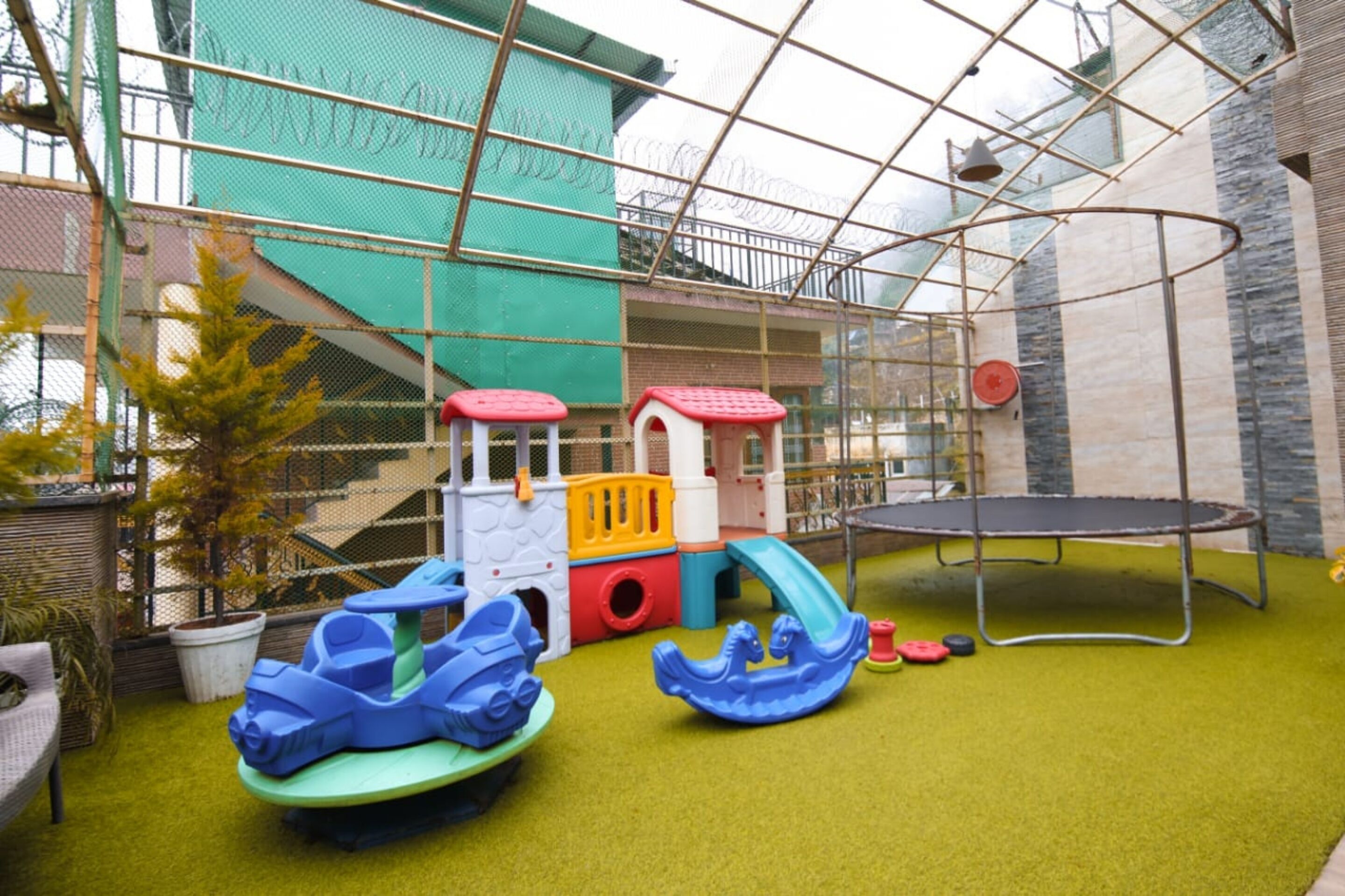 An indoor play area with a trampoline, colorful play structures, and artificial turf.
