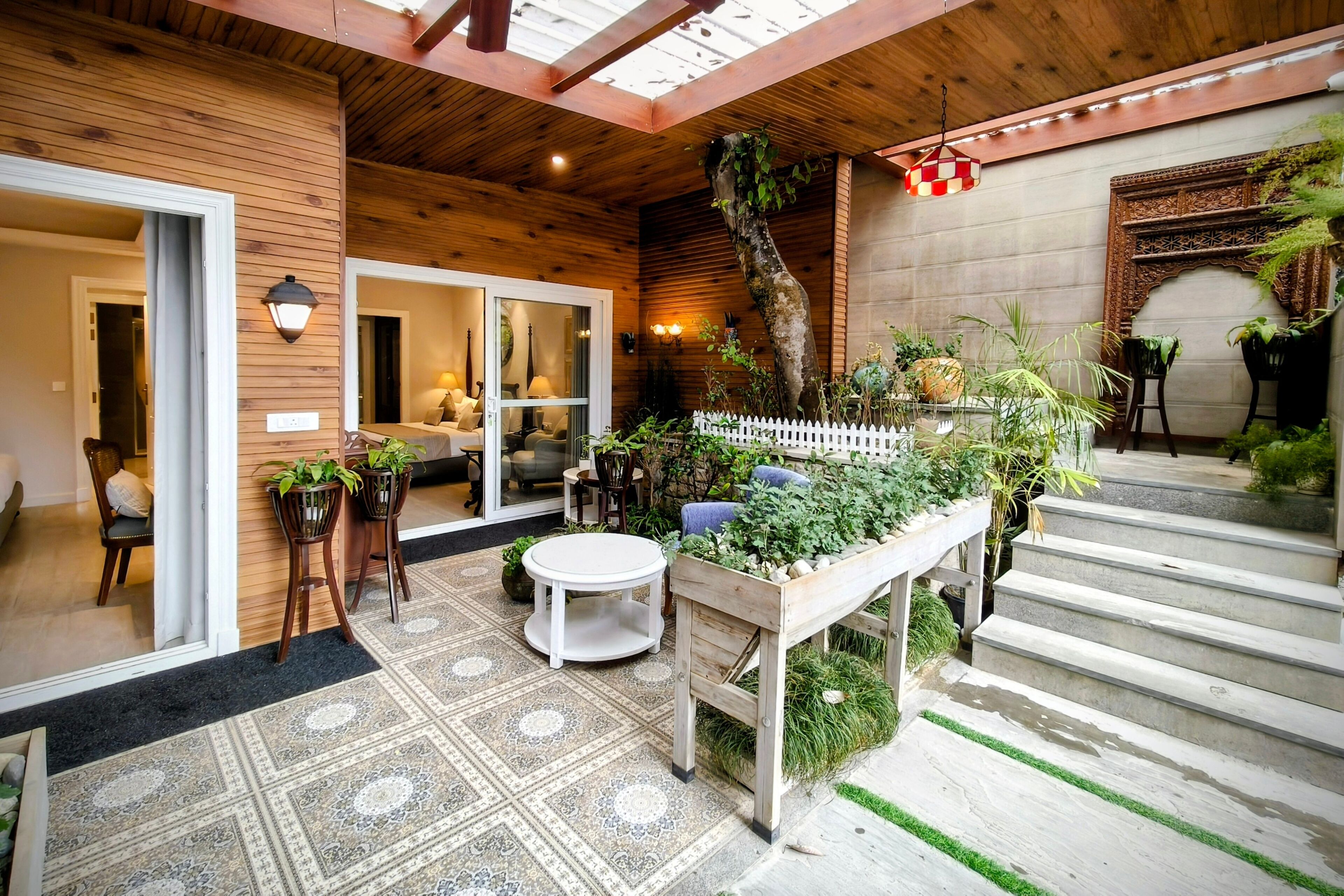 Une façade en bois, une terrasse couverte, une table ronde blanche et un banc en bois agrémenté de plantes.