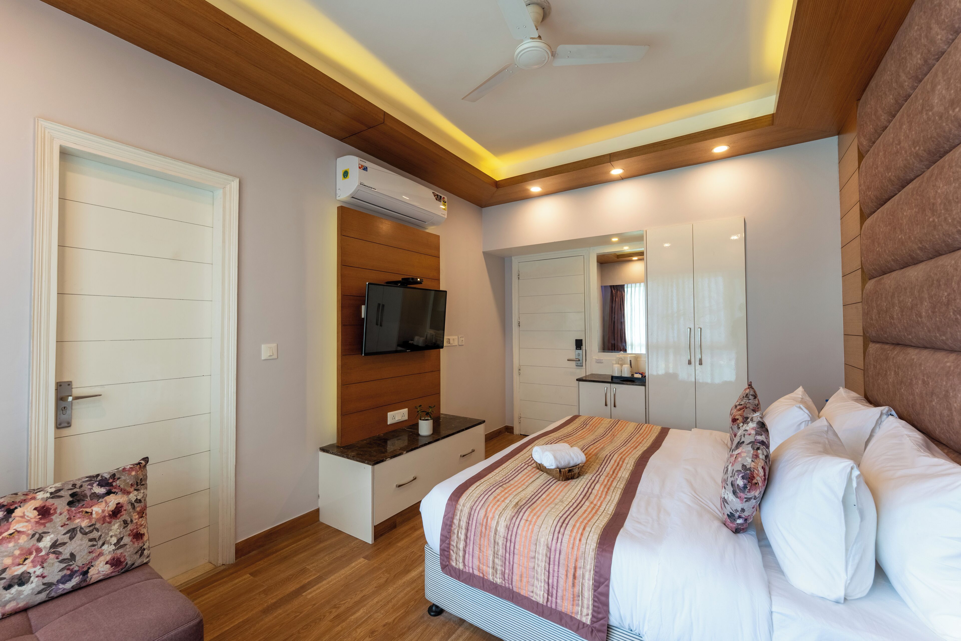 A modern bedroom with a wooden ceiling, a bed with a striped blanket, a flat-screen TV, and a built-in air conditioning unit.