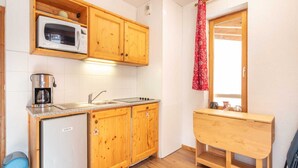 Una cocina compacta con armarios de madera, microondas, cafetera y refrigerador pequeño.