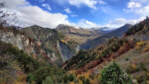 Paisaje montañoso con un valle, árboles de colores otoñales y cielo despejado.
