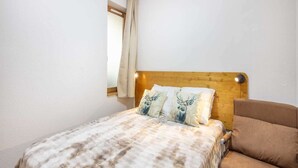 Un dormitorio con cabecera de madera, una cama con ropa de cama estampada, un sillón marrón y una ventana con cortina.