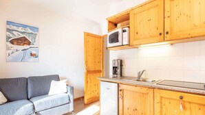 Una cocina compacta con armarios de madera, microondas, cafetera y refrigerador.
