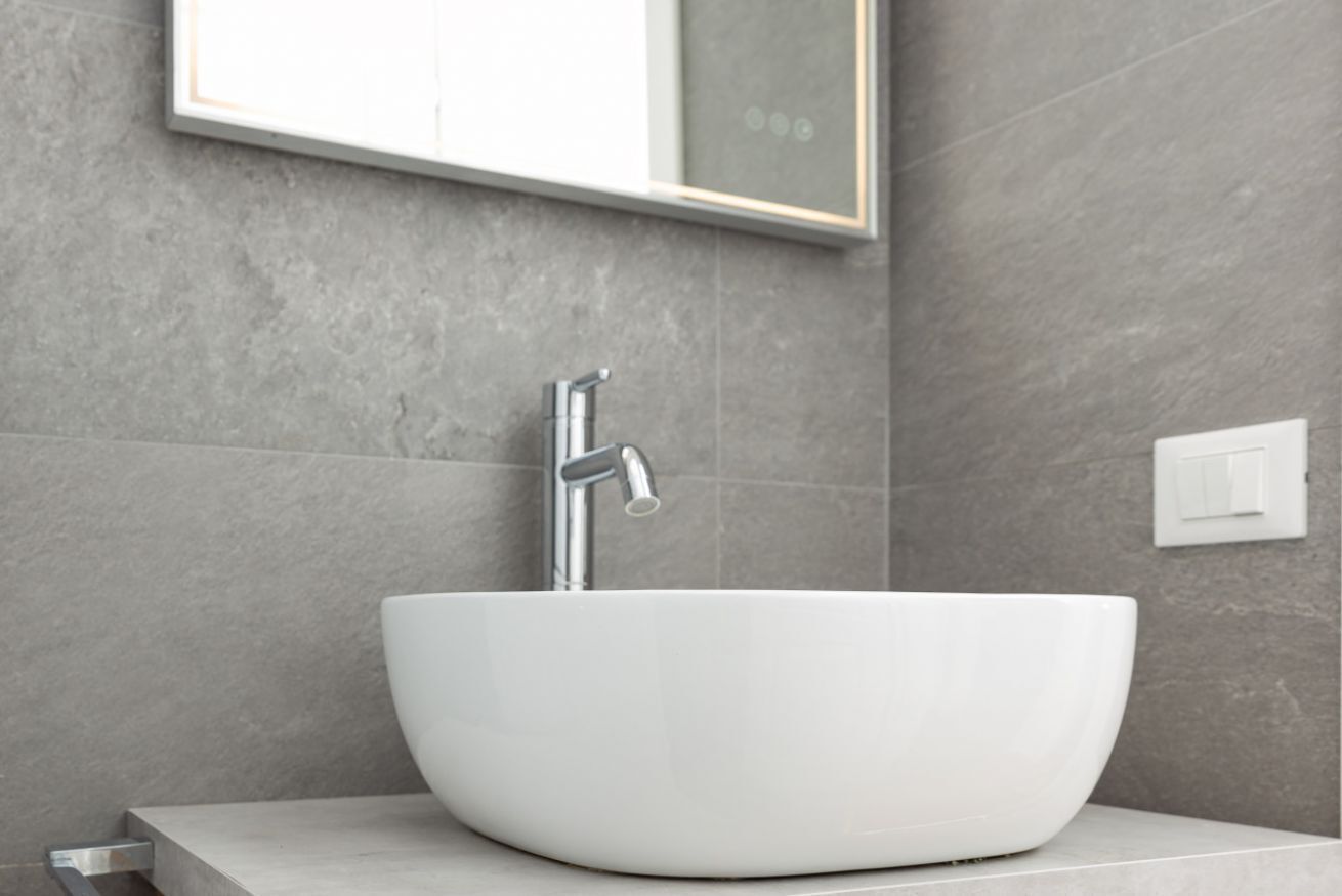 A modern bathroom with a white vessel sink, a chrome faucet, and a mirror above it.