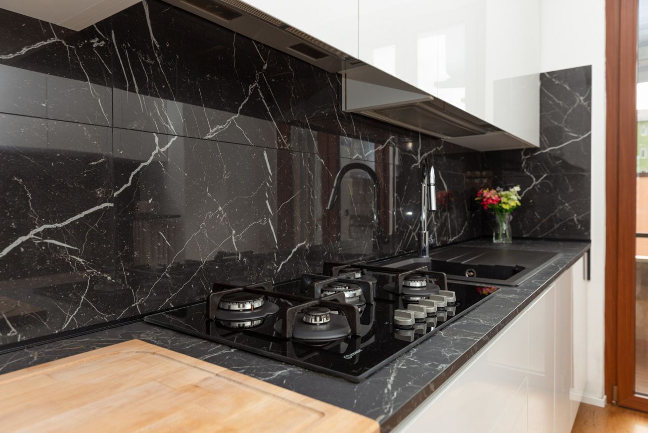 A modern kitchen with black marble countertops, a gas stove, and a stainless steel range hood.