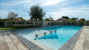 A rectangular swimming pool with a wooden deck surrounding it, a metal fence, and a clear blue sky in the background.