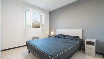 A bedroom with a bed, a nightstand, a drawer unit, a window, and a ceiling light.