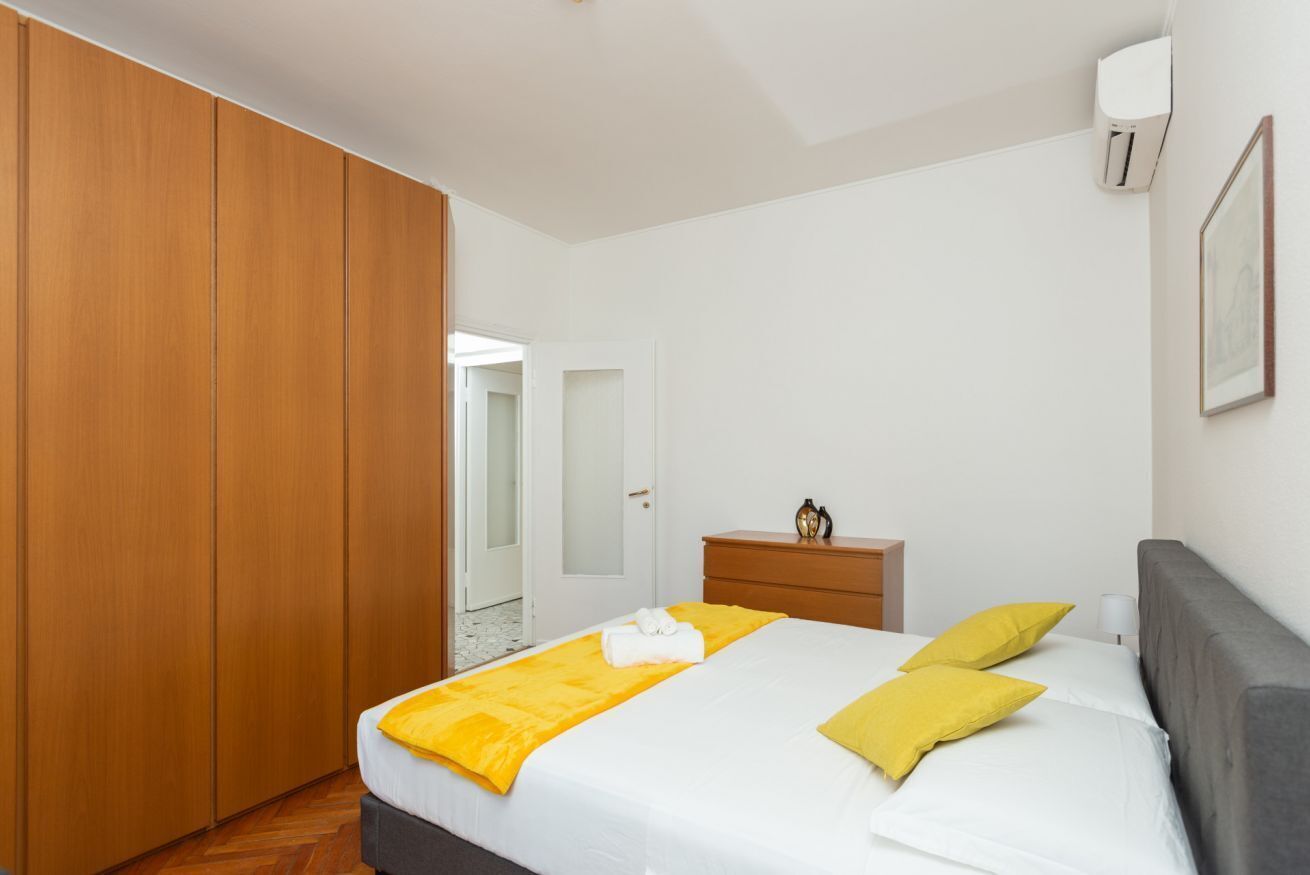 A bedroom with a bed, wooden wardrobe, bedside table, and an air conditioning unit.