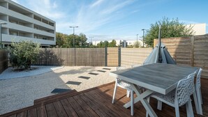 A patio area with a wooden deck, a table and chairs, and a view of a modern building in the background.