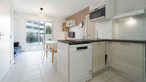 A modern kitchen with a dishwasher, microwave, and built-in oven. There is a dining area with a table and chairs, and a view of a balcony.