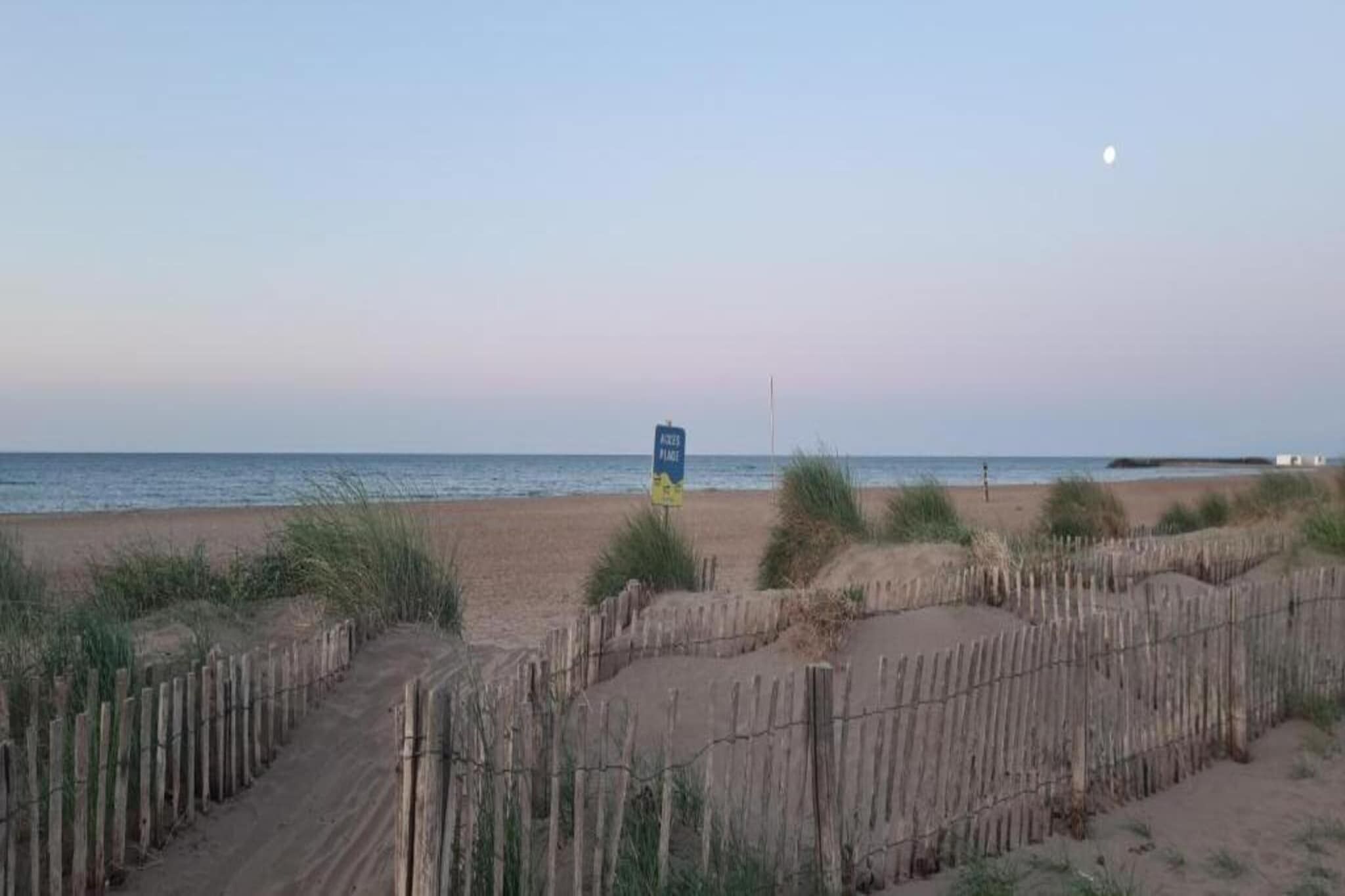 Une plage avec une clôture en bois et un panneau visible au loin.