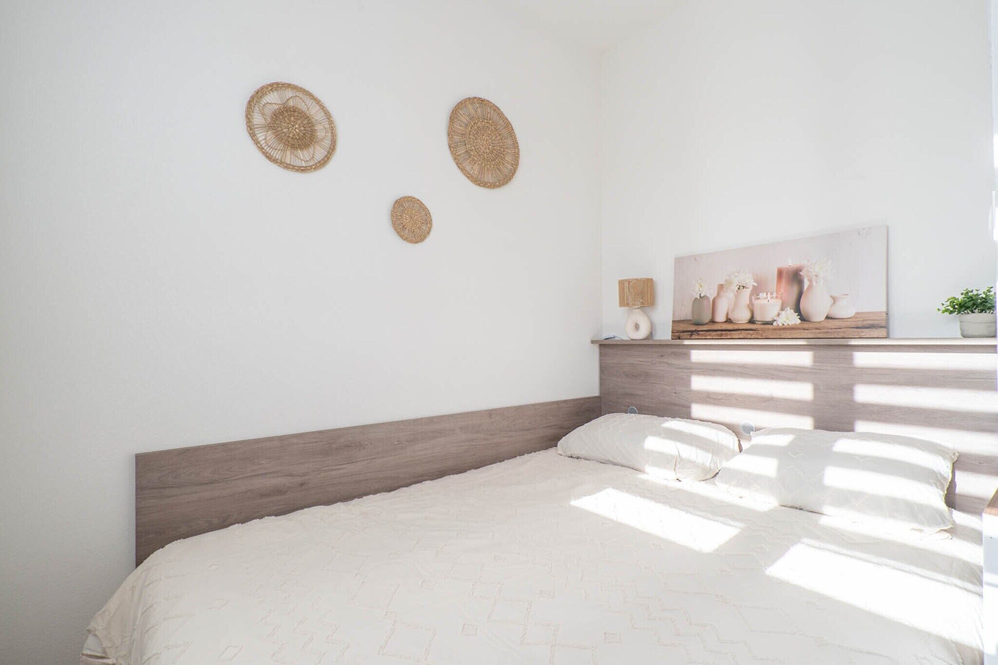 A bedroom with a wooden headboard, a bed with a white quilt, and wall-mounted woven decorations.