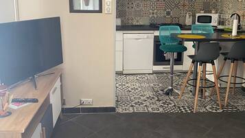 A compact kitchen with a microwave, stove, and modern appliances. There is a dining area with a small table and chairs, and a TV in the corner.