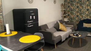 A modern living room with a grey sofa, a black cabinet, a dining table with yellow placemats, teal chairs, and a patterned wall. - Zahra D'or (Plombières-lès-Dijon)