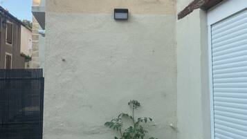 A small outdoor seating area with a table and chairs, a potted plant, and a wall-mounted device.