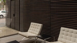 Un área de estar moderna al aire libre con dos sillones acolchados y una pequeña mesa, frente a un fondo de listones horizontales de madera.