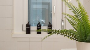Un baño con ventana, una planta y tres botellas de jabón corporal, champú y acondicionador.