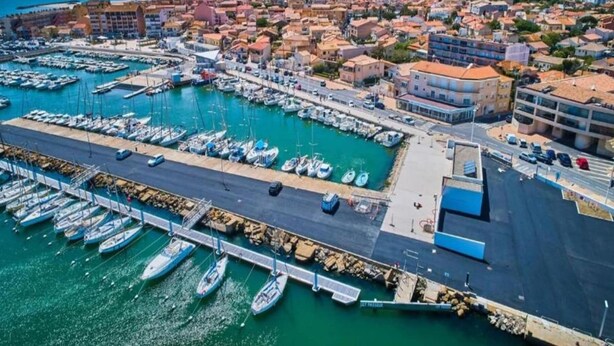 Vista aèria d'una localitat costanera amb un port esportiu, edificis i un cel serè.