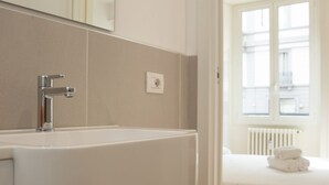 A bathroom with a white sink, a mirror, and a window with a view of buildings. - Klimt Central station - Two Room Apartment (Milano)