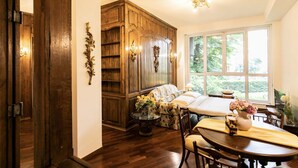 Una habitación con un armario de madera, una cama con colcha azul y blanca, una mesa de comedor con sillas y una ventana con vistas a la vegetación.