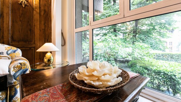 Una mesa de madera con un cuenco decorativo, una lámpara y vistas al verdor a través de una ventana.