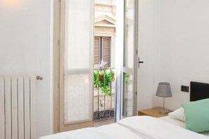 A hotel room with a bed, a nightstand with a lamp, and a view of a balcony with plants.