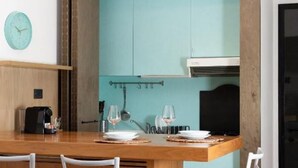 A dining area with a wooden table set for two, a clock on the wall, and teal cabinetry. - Mint - Van Gogh - Dome Cathedral (Milano)