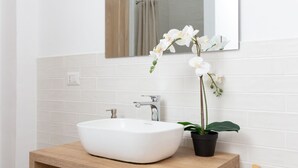 A bathroom with a white sink, a mirror, and a potted orchid. - New Exclusive Melegnano Apartments- Near train station X4 (Melegnano)
