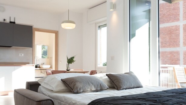 A modern bedroom with a large bed, a desk, and a view of a brick wall.