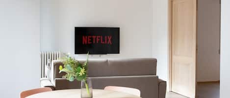 A modern living room with a round table, a sofa, and a TV mounted on the wall displaying "NETFLIX".