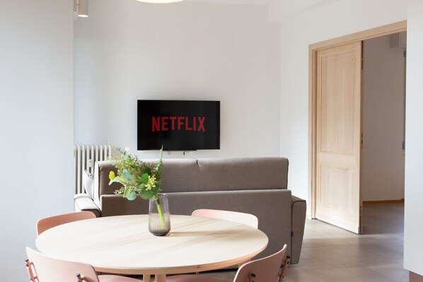 A modern living room with a round table, a sofa, and a TV mounted on the wall displaying "NETFLIX".