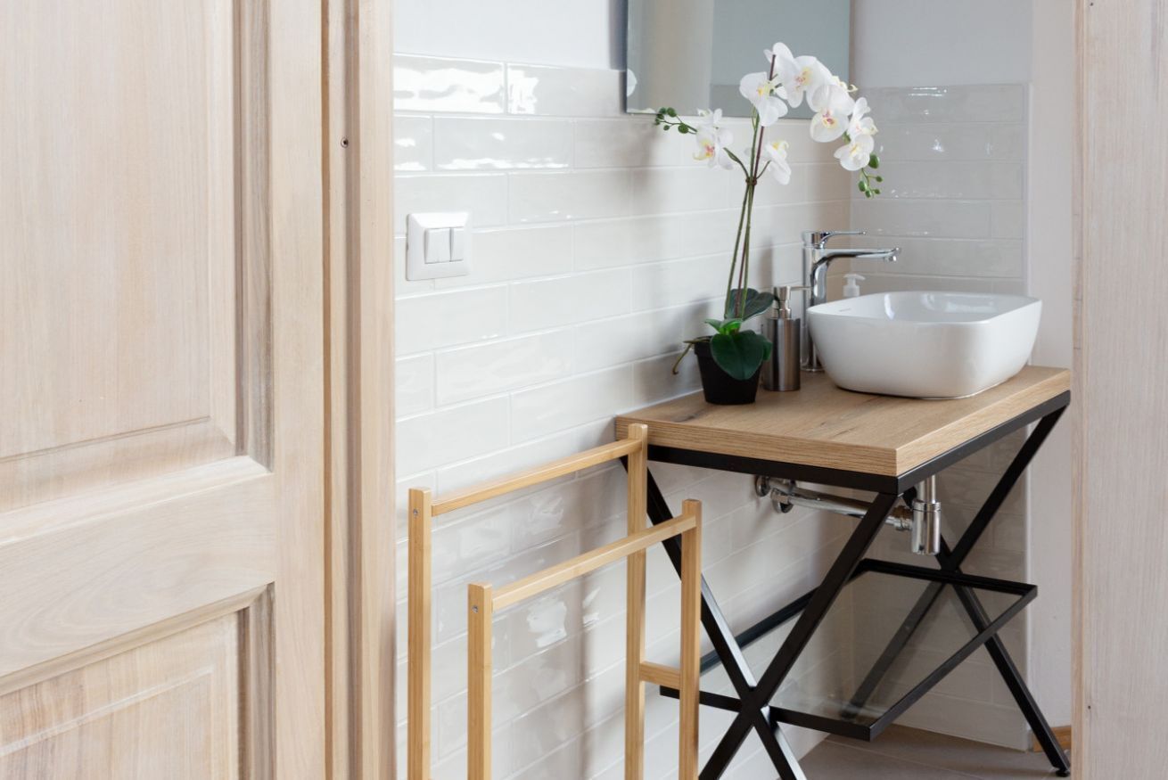 Un baño con un lavamanos blanco, un espejo y una orquídea en maceta.